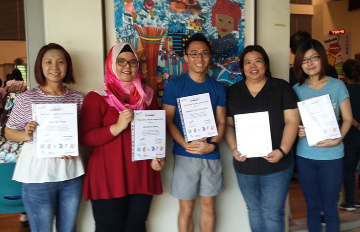 Five people stand together smiling, each holding a certificate, in front of a colorful mural.